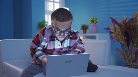 Young-man-with-dwarfism-doing-focused-and-serious-work-at-home-at-night-using-laptop.